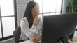 © Krakenimages.com - Woman working in modern office, focused on computer screen with thoughtful expression, surrounded by bright daylight and sleek interior decor, emphasizing professional setting