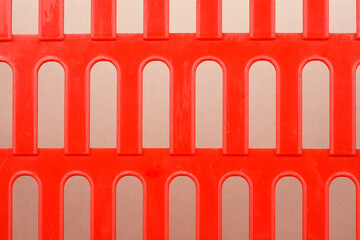 a close-up shows a section of a bright red plastic mesh or grating with repeating arched openings