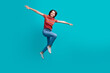 © deagreez - Happy Young Woman in Casual Outfit Jumping Against a Bright Turquoise Background Expressing Joy and Positivity