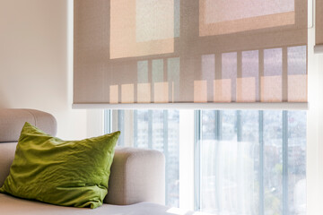 Poster - Beige roller blinds, close-up view, covers a large window, softly filtering sunlight and casting geometric shadows. Sunscreen fabric of roller shades creates a cozy feel in the bright interior space.