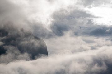 Wall Mural - Panorama of a rugged mountain exposed between mist and clouds with partially transparent sky