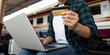 © Natee Meepian - Travel and Finance. An excited traveler holding a credit card while working on his laptop at the train station.