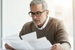 © Anjali - A mature man with glasses carefully reviews important documents, concentrating on details.