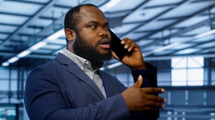 Poster - Close up shot of programmer in data center talking in phone call, doing inspection. On field IT specialist talking with manager in server hub during telephone call, monitoring mainframes, camera A
