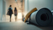 © ABF_MATEO - Yoga mat rolled up with a towel in a hallway, two people walk towards a light at the end of the hall.