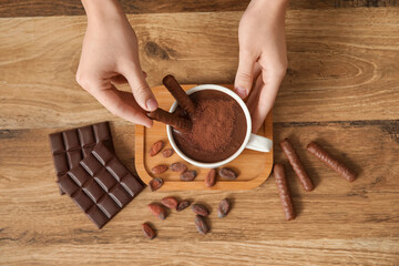 Wall Mural - female hands with chocolate sticks and cup of melted chocolate on wooden table in kitchen. top view