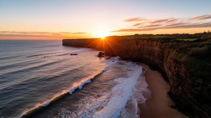 Poster - Aerial view of a dramatic coastal landscape featuring cliffs sea and beach under a vibrant sunset sky with golden light reflecting on the water
