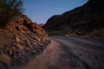 Poster - A rugged dirt road winds through a canyon under a twilight sky. The scene is defined by earthen tones of the rock formations and road contrasting with a soft blue gradient of the sky