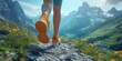 © supattra - Close-up of a woman's legs in running shoes walking on a mountain trail, with a panoramic view of mountains and a natural background.