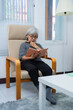 © Tj - Relaxed elderly woman enjoying reading a book while sitting comfortably in an armchair in her living room, creating a peaceful and cozy atmosphere