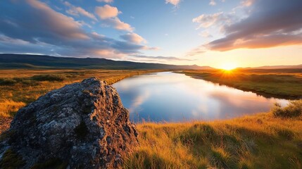 Poster - Scenic landscape with golden sunset over a calm lake and surrounding fields of grass. The sky is filled with clouds and a warm glow of the setting sun casting reflections in the water