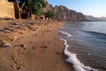 Poster - Scenic beach landscape featuring a sandy shore with gentle waves meeting the water edge at daytime in golden light with mountain view