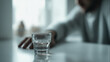 © Inspire Shots Hub - Close-up of a glass of liquid on table, blurred person in background, suggesting loneliness or contemplation.  Image evokes feelings of isolation and introspection.