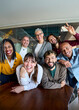 © CarlosBarquero - Vertical. Multicultural coworkers laughing during a lively office meeting, showcasing teamwork, friendship, success, and a vibrant corporate atmosphere.