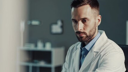 Aufkleber - Male doctor concentrating while working on computer, seated at desk inside modern medical office, wearing white professional attire