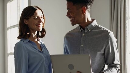 Aufkleber - Two business colleagues, a woman and a man, are standing together, looking at a laptop and sharing a moment of laughter and camaraderie in a sunlit office space