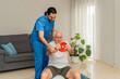 © Renata Hamuda - Male Physiotherapist in blue uniform assisting senior man exercising with weights and fitness ball at home