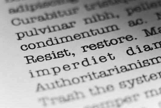 Resist and restore. Text printed on a page. A piece of paper with a phrase written in retro typewriter font.