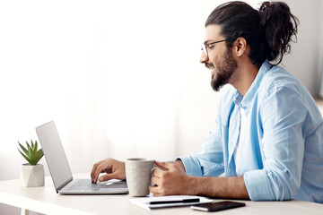 Aufkleber - Remote Work. Handsome Male Freelancer Using Laptop And Drinking Coffee, Working Remotely At Home Office, Sitting At Desk Near Window, Browsing Internet, Having Online Job, Side View With Copy Space