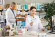 © JackF - Female pharmacist in uniform looking for medicine in pharmacy using computer. In the background, male pharmacist places