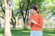 © Thitisak - Asian woman walks and listens to music in a public park.