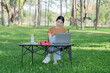 © Thitisak - Asian woman sitting using laptop, working in a park