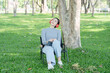 © Thitisak - An Asian woman sits listening to music in a park.
