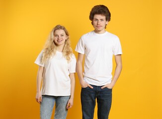 Wall Mural - young woman and man wearing blank white t-shirts on orange background. mockup for design