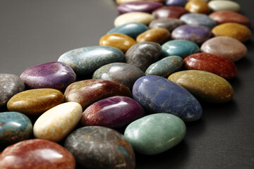 Poster - Close-up of multicolored polished stones arranged in a row on dark background, showcasing a smooth and glossy texture symbolizing balance, nature, and serenity