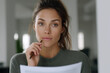 © SerPak - Thoughtful young caucasian female reviewing document in office setting.