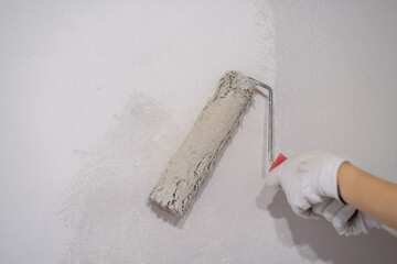 Poster - A woman manually paints a wall with a paint roller. Painting the apartment