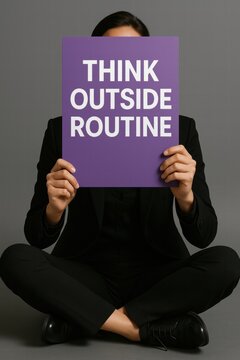 A person in a black suit seated on the floor holds a purple sign reading 