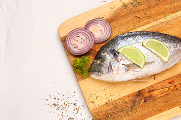 Wall Mural - Wooden board of raw dorado fish with lemon and onion on light background