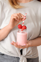 Wall Mural - Woman holding mason jar of tasty strawberry smoothie on light background