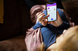 © Geber86 - Pregnant woman using mobile banking app while relaxing on couch