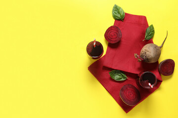Wall Mural - Glasses of fresh beet juice with basil and vegetables on yellow background