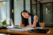 © Wasana - A woman is sitting at a desk with a laptop and papers
