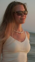 Wall Mural - young woman with long hair walking on beach at sunset with golden reflections on sea water. vertical