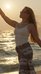 Wall Mural - young woman with long hair enjoying sunset at beach with golden reflections on sea water. vertical v