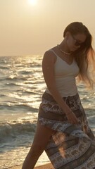 Wall Mural - young woman with long hair enjoying sunset at beach with golden reflections on sea water. vertical v