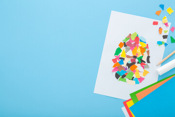 Wall Mural - Glued easter egg shape with colorful torn application paper pieces on white paper. Pastel blue table background. Development task for little kid motor skills. Empty place for text. Top down view.