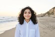 © Elena - A joyful woman stands on a sandy beach, smiling as gentle waves lap at her feet. The clear sky reflects a peaceful sunset atmosphere