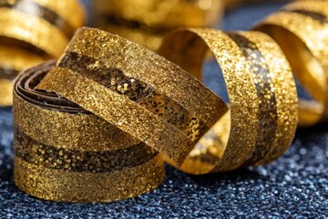 Poster - Gold glitter streamers curl elegantly on a dark textured surface, perfect for festive decorations at parties and celebrations