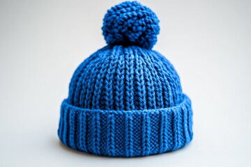 Poster - Warm blue knitted beanie with pom-pom displayed on a neutral background during winter season