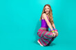 Stylish young woman in vibrant outfit smiling playfully on turquoise background, showcasing retro fashion