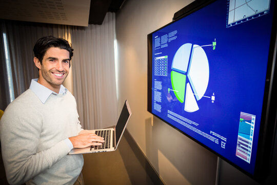 Man holding laptop and presenting pie chart data on wall display in modern office, copy space