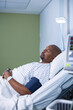 © WavebreakMediaMicro - African American man lying in hospital room, with blood pressure cuff and bedside lamp