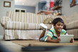 © wavebreak3 - 6-year-old boy lying on woven rug in living room, holding white tablet and smiling