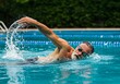 © GS-Studio - An older man is seen swimming with a forward stroke in a bright blue pool