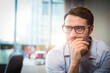 © WavebreakMediaMicro - Man wearing eyeglasses sitting at desk in office with skyline, holding pen near mouth, copy space